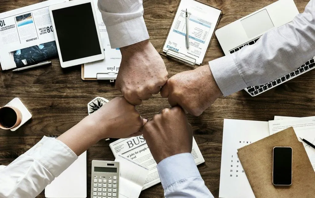 Vier Fäuste verschiedener Kollegen treffen sich über dem Schreibtisch – Zusammenhalt im Team als Ziel des AGG